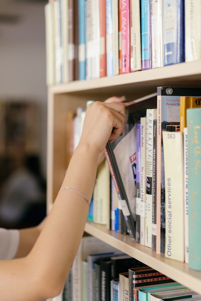 A hand reaching for a book on a library shelf, representing education and knowledge.